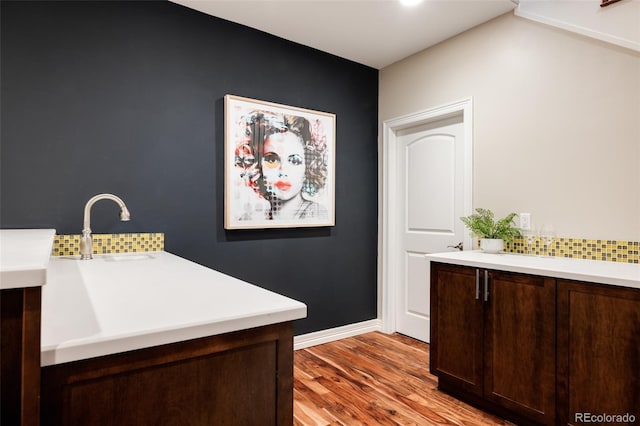 bar featuring baseboards, tasteful backsplash, a sink, and light wood-style floors