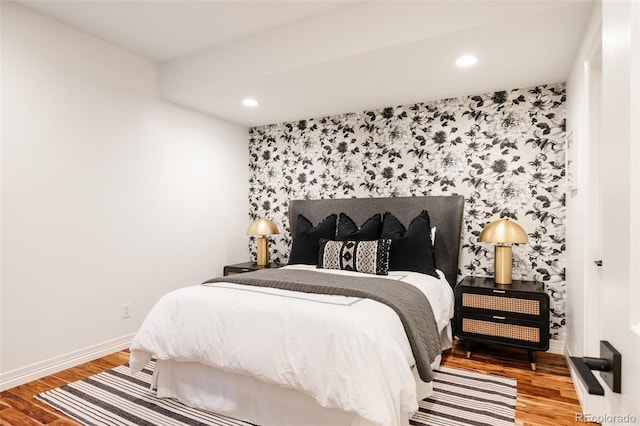 bedroom with an accent wall, baseboards, wood finished floors, and recessed lighting