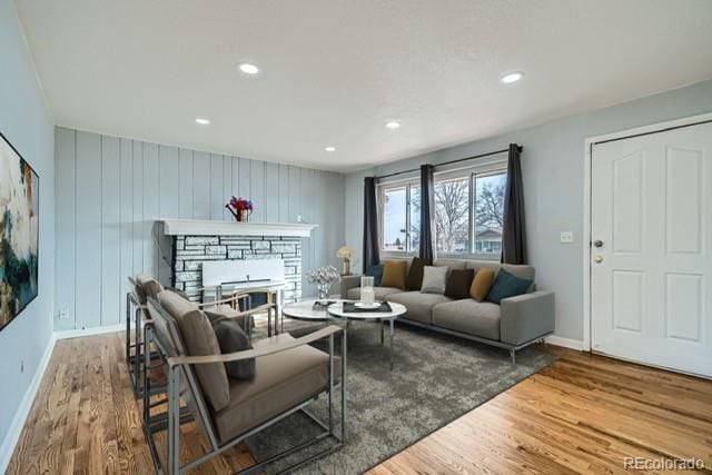 living room featuring a stone fireplace, recessed lighting, wood finished floors, and baseboards