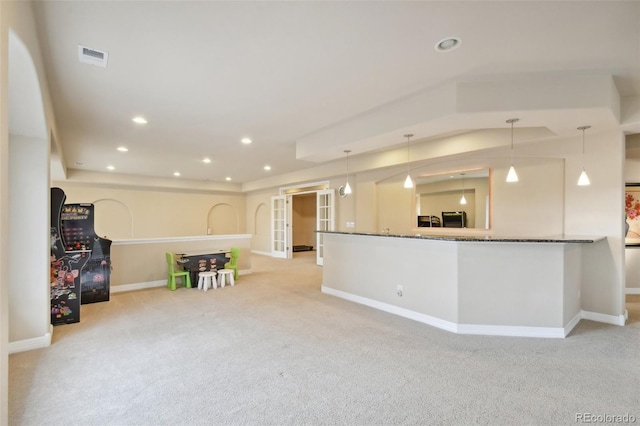 kitchen with light colored carpet, hanging light fixtures, and dark stone counters