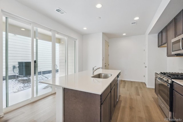 kitchen with a kitchen island with sink, sink, light hardwood / wood-style flooring, dark brown cabinetry, and stainless steel appliances