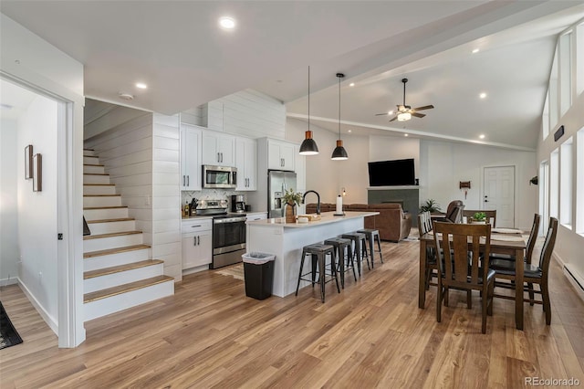 kitchen featuring white cabinetry, ceiling fan, stainless steel appliances, vaulted ceiling, and a kitchen island with sink