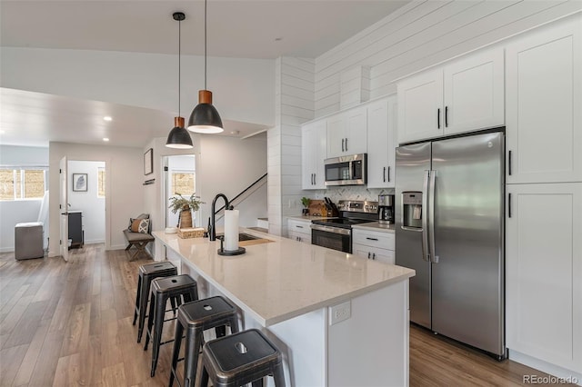 kitchen with a kitchen island with sink, pendant lighting, white cabinets, and stainless steel appliances