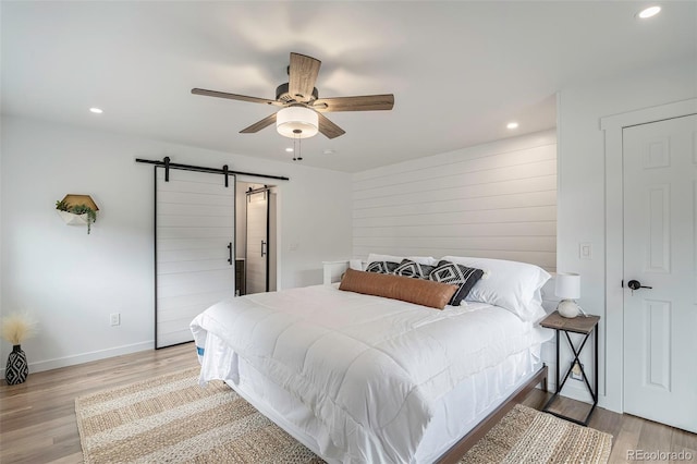 bedroom with ceiling fan, a barn door, and light hardwood / wood-style floors