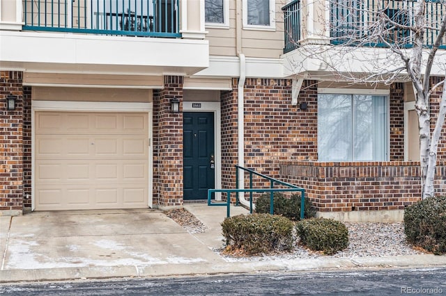 view of exterior entry with a garage, brick siding, concrete driveway, and a balcony