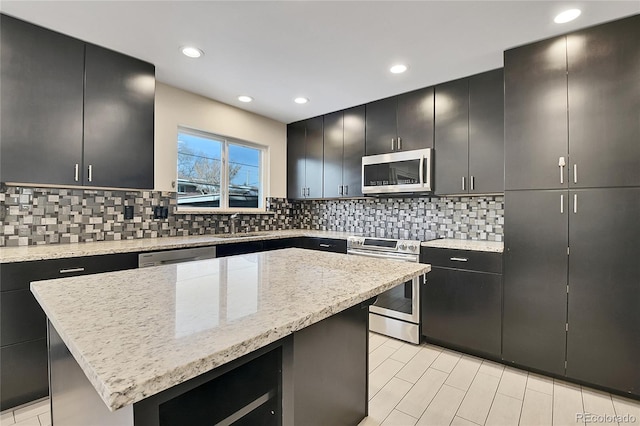 kitchen with sink, appliances with stainless steel finishes, a kitchen island, light stone countertops, and backsplash