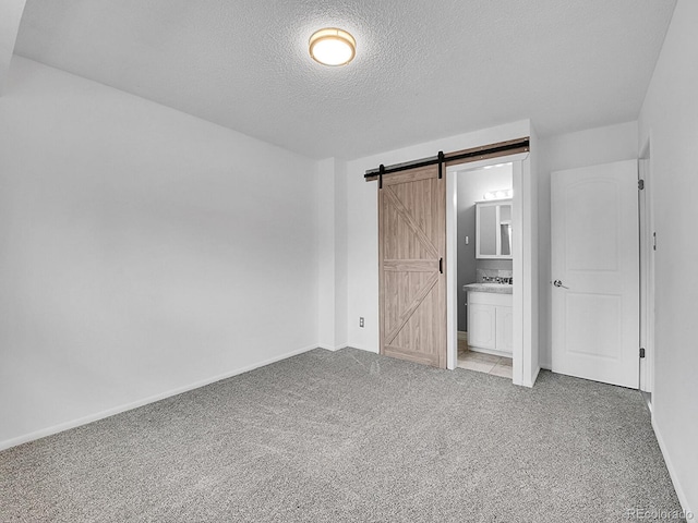 unfurnished bedroom with a barn door, light colored carpet, connected bathroom, and a textured ceiling