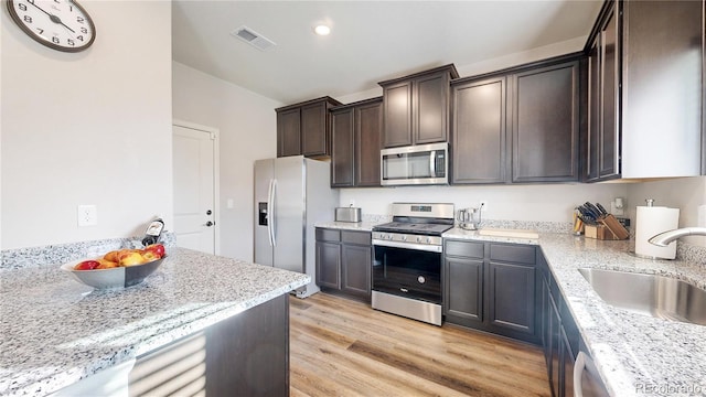 kitchen with dark brown cabinetry, light hardwood / wood-style flooring, light stone counters, sink, and appliances with stainless steel finishes