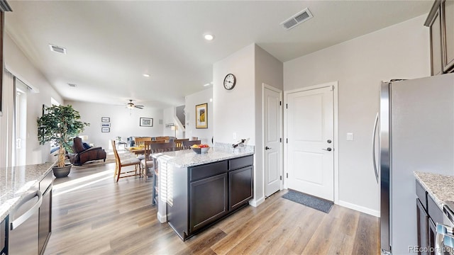 kitchen featuring light wood-type flooring, light stone counters, ceiling fan, and stainless steel refrigerator