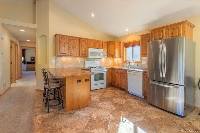 kitchen featuring sink, white appliances, a breakfast bar, decorative backsplash, and kitchen peninsula