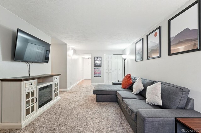 living area featuring light colored carpet, baseboards, and a textured ceiling