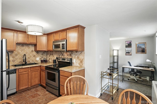 kitchen featuring stainless steel appliances, a sink, light countertops, tasteful backsplash, and brown cabinets