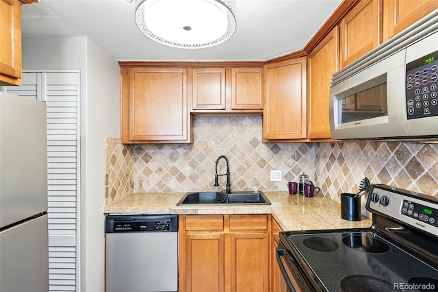 kitchen featuring appliances with stainless steel finishes, a sink, tasteful backsplash, and brown cabinetry