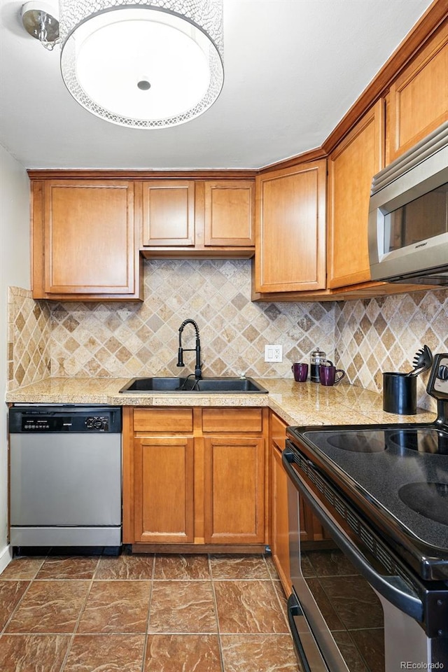 kitchen with appliances with stainless steel finishes, a sink, light countertops, tasteful backsplash, and brown cabinetry