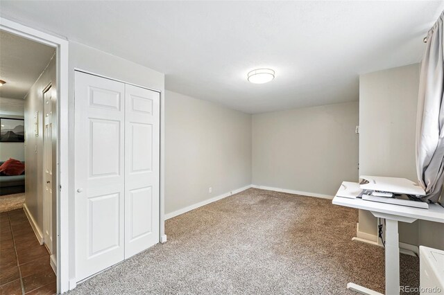 unfurnished bedroom featuring baseboards, dark carpet, and a closet