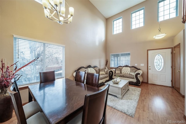 dining room featuring a notable chandelier, a towering ceiling, and light hardwood / wood-style flooring