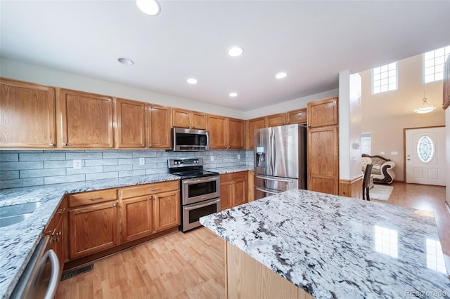 kitchen with appliances with stainless steel finishes, backsplash, light hardwood / wood-style flooring, and light stone counters