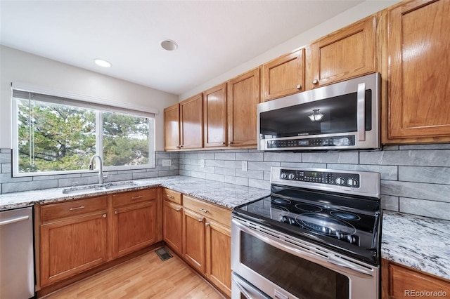 kitchen featuring backsplash, light stone countertops, sink, and appliances with stainless steel finishes