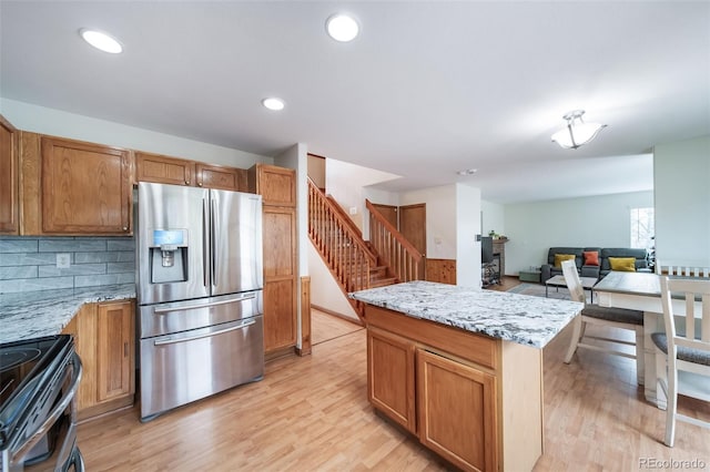 kitchen featuring tasteful backsplash, light stone counters, light hardwood / wood-style flooring, stainless steel fridge with ice dispenser, and black range with electric stovetop