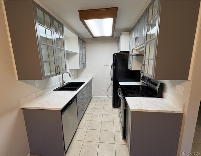 kitchen featuring light tile patterned flooring, gray cabinetry, a sink, appliances with stainless steel finishes, and glass insert cabinets