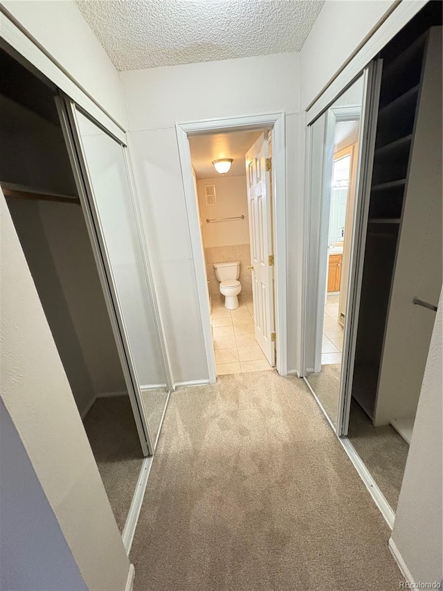 corridor featuring light carpet, light tile patterned floors, and a textured ceiling