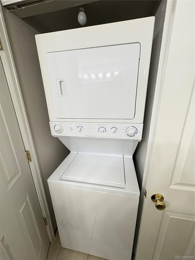 clothes washing area with laundry area, light tile patterned floors, and stacked washer and clothes dryer