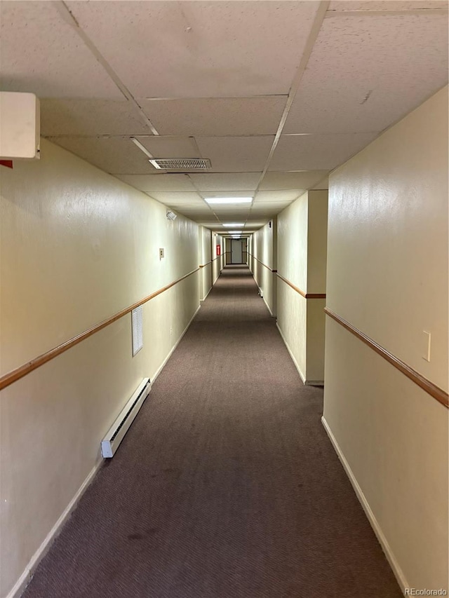 corridor with dark colored carpet, visible vents, a paneled ceiling, and baseboard heating