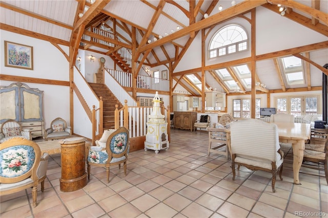 dining room with a skylight, high vaulted ceiling, tile patterned flooring, beamed ceiling, and stairs