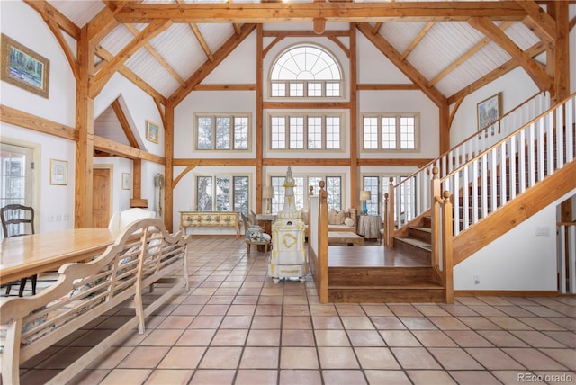 unfurnished living room featuring light tile patterned floors, beamed ceiling, a high ceiling, and stairway