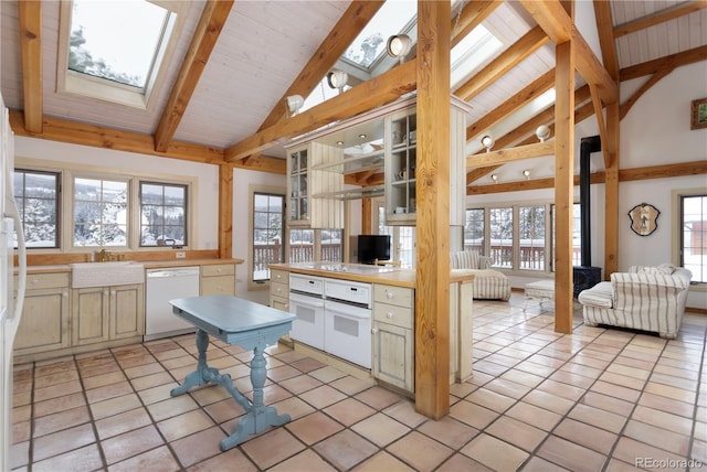 kitchen featuring white appliances, a skylight, light tile patterned floors, a sink, and beam ceiling