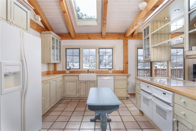 kitchen featuring vaulted ceiling with skylight, white appliances, a sink, light countertops, and glass insert cabinets