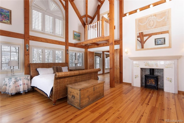 bedroom featuring a wood stove, light wood-style floors, multiple windows, and a high ceiling