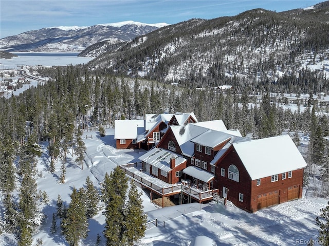 snowy aerial view featuring a mountain view and a wooded view