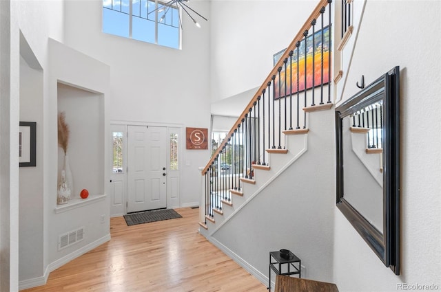 foyer featuring visible vents, an inviting chandelier, stairs, wood finished floors, and a high ceiling