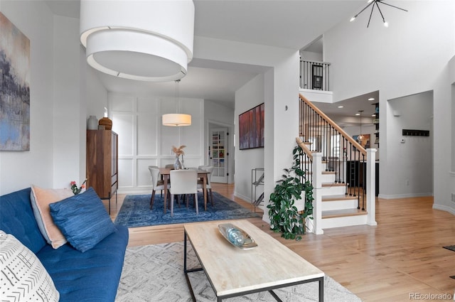 living area featuring stairs, a towering ceiling, wood finished floors, baseboards, and a chandelier