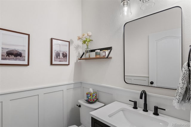 bathroom with vanity, toilet, wainscoting, and a decorative wall