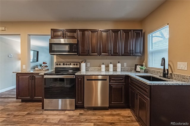 kitchen with dark brown cabinets, sink, light stone countertops, hardwood / wood-style floors, and stainless steel appliances