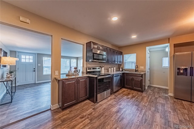 kitchen featuring sink, dark wood-type flooring, stainless steel appliances, light stone countertops, and dark brown cabinetry