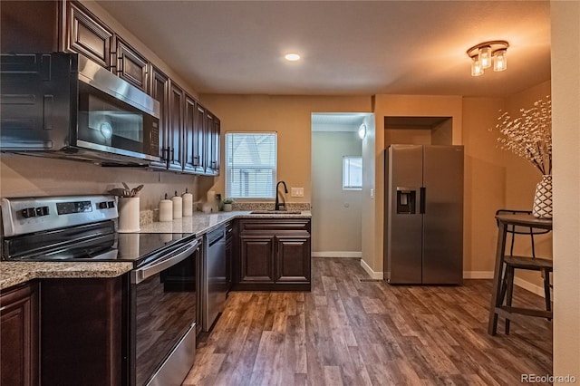 kitchen featuring light stone countertops, stainless steel appliances, sink, hardwood / wood-style flooring, and dark brown cabinets