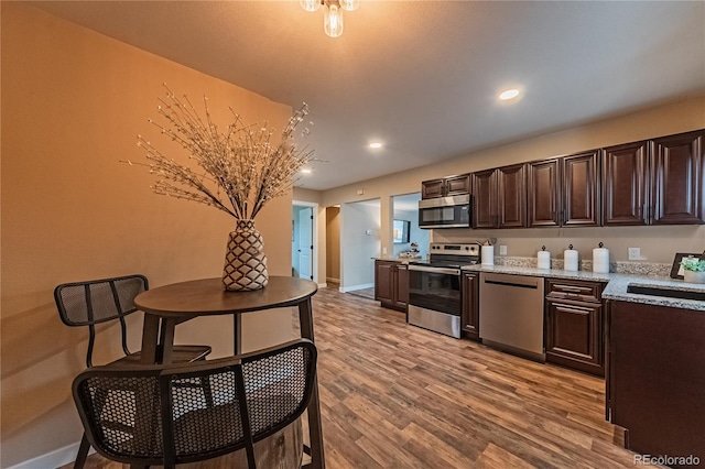 kitchen featuring dark brown cabinetry, appliances with stainless steel finishes, light hardwood / wood-style floors, sink, and light stone counters