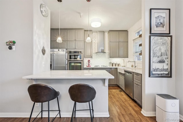 kitchen with appliances with stainless steel finishes, pendant lighting, gray cabinetry, a kitchen breakfast bar, and wall chimney range hood