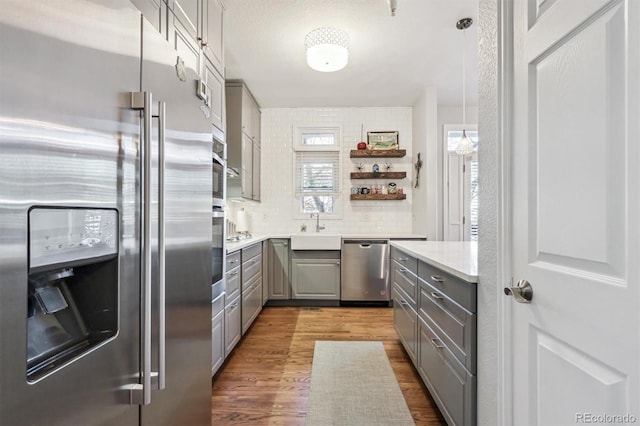 kitchen featuring sink, gray cabinetry, pendant lighting, stainless steel appliances, and hardwood / wood-style floors