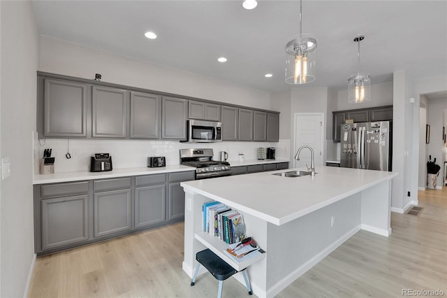 27853 E 8th Ave, Aurora, CO 80018 - kitchen featuring appliances with stainless steel finishes, light wood finished floors, gray cabinets, tasteful backsplash, and a kitchen island with sink
