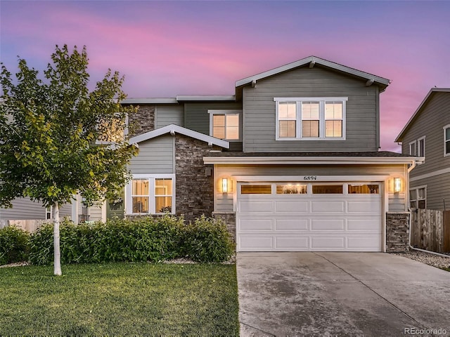 traditional-style house featuring a lawn, stone siding, fence, concrete driveway, and an attached garage