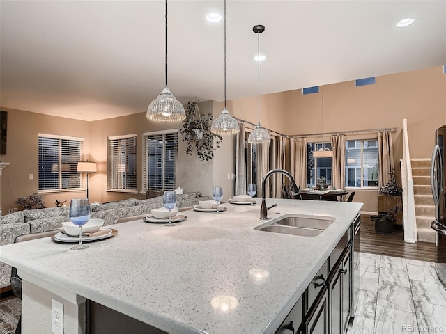 kitchen with marble finish floor, a center island with sink, a sink, light stone counters, and open floor plan