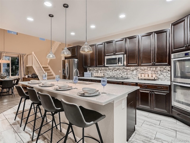 kitchen with backsplash, a center island with sink, appliances with stainless steel finishes, a kitchen breakfast bar, and a sink