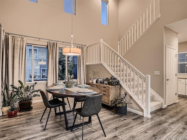 dining room featuring a towering ceiling, baseboards, wood finished floors, and stairs