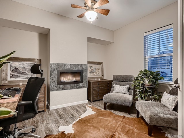 office space featuring a ceiling fan, wood finished floors, baseboards, and a lit fireplace