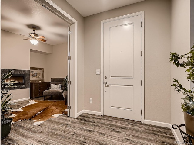 foyer with dark wood-style floors, a fireplace, baseboards, and a ceiling fan