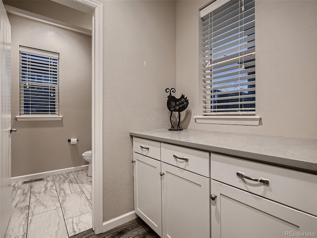 bathroom with baseboards, toilet, a textured wall, marble finish floor, and vanity